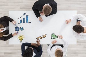 Överblick av fem personer runt ett bord som ritar symboler för affärsutveckling.